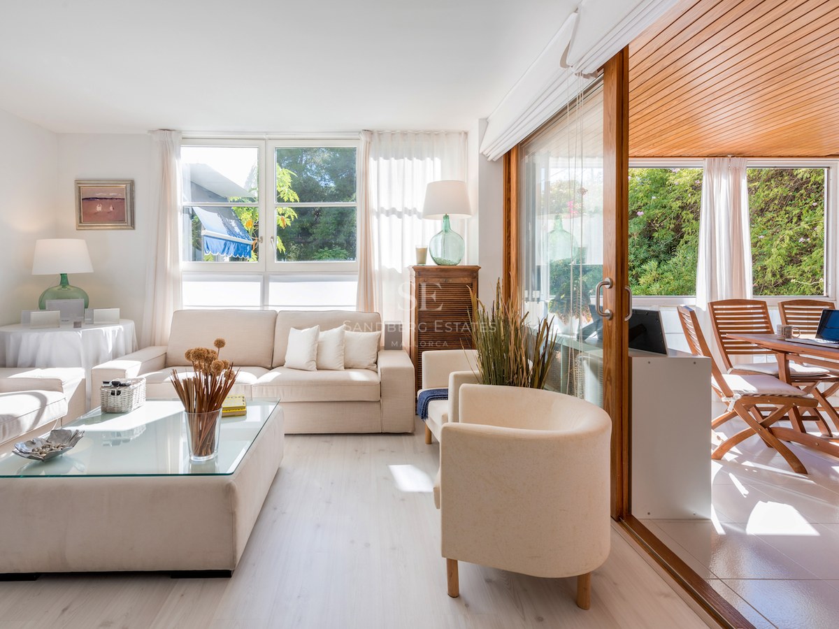 Salon lumineux avec canapés crème et grandes baies vitrées ouvrant sur une terrasse en bois.