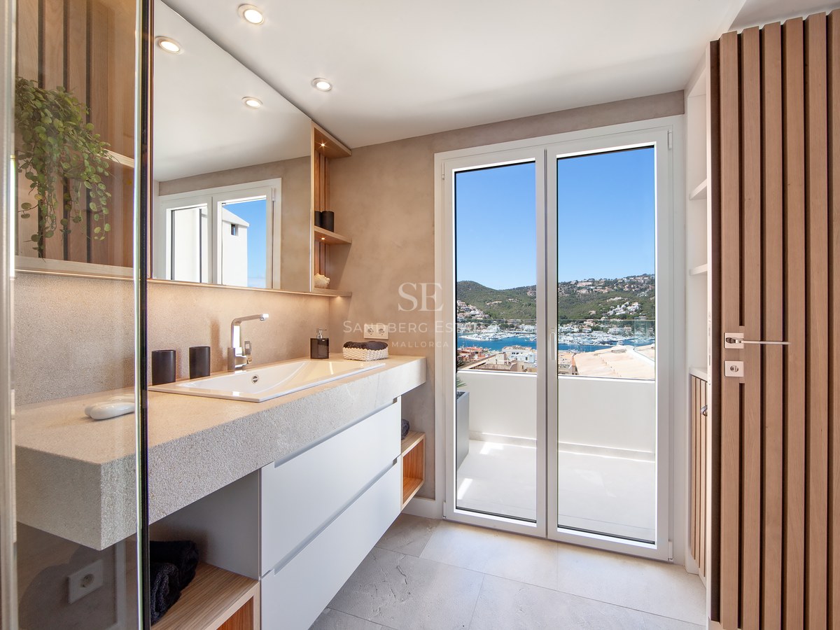 Modern bathroom with stone vanity, large mirror, and glass doors opening to a balcony with a marina view.