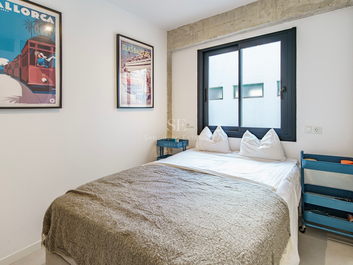 Chambre moderne avec lit double, poutres en béton, dessertes bleues et affiches de voyage vintage.