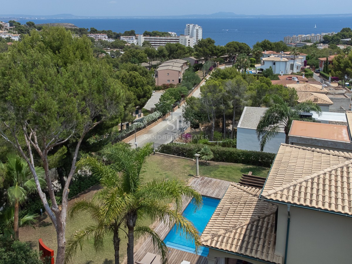 Vue surélevée d'une piscine et de toits en terre cuite avec la mer Méditerranée et la côte à l'horizon.