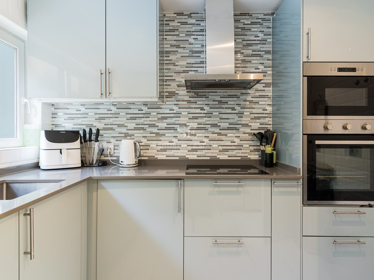 Modern kitchen featuring light blue cabinets, grey countertops, a mosaic tile backsplash, and stainless steel appliances.