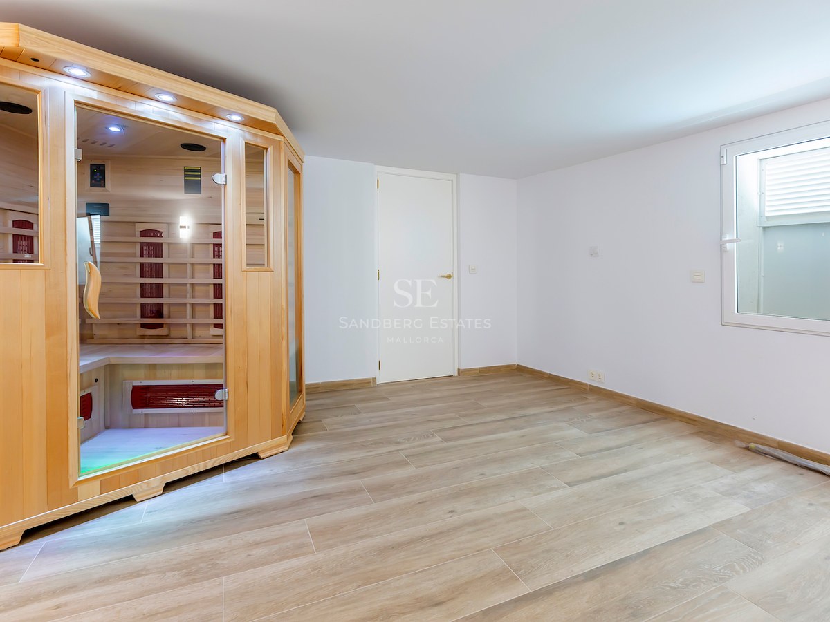 Modern indoor room featuring a light wood sauna cabin with glass doors and wood-effect tile flooring.