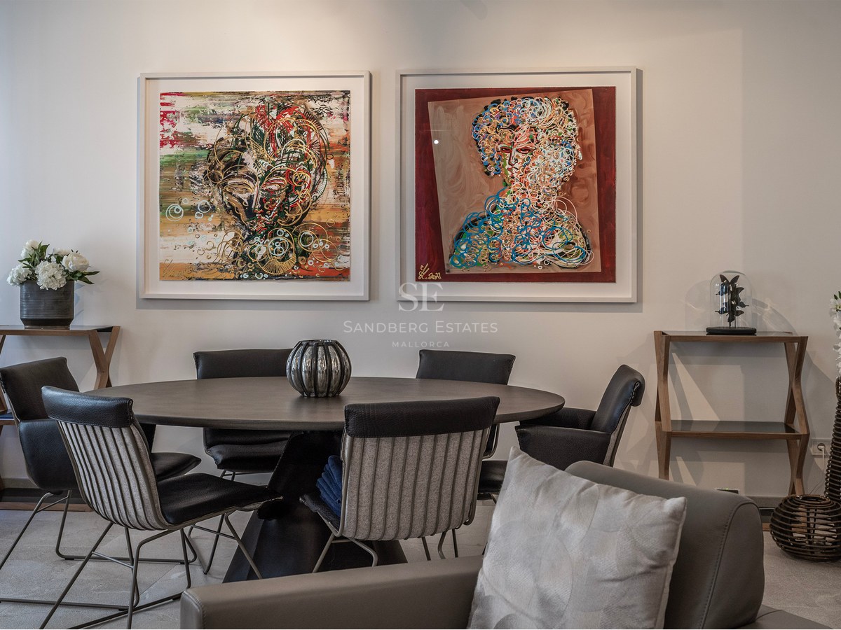 Modern dining room featuring a dark round table, designer chairs, and two large abstract paintings on a white wall.