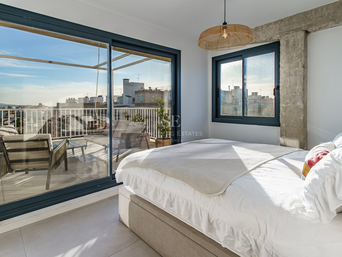 Chambre lumineuse avec lit blanc et grandes baies vitrées coulissantes ouvrant sur une terrasse privée avec vue.