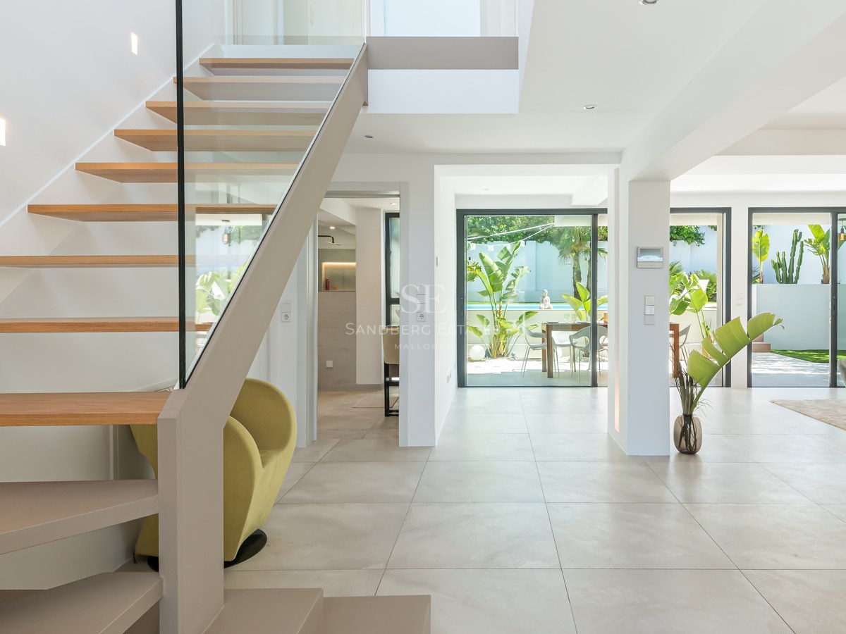 Modern hallway featuring a wooden floating staircase with glass railings, leading to an open living space and garden.