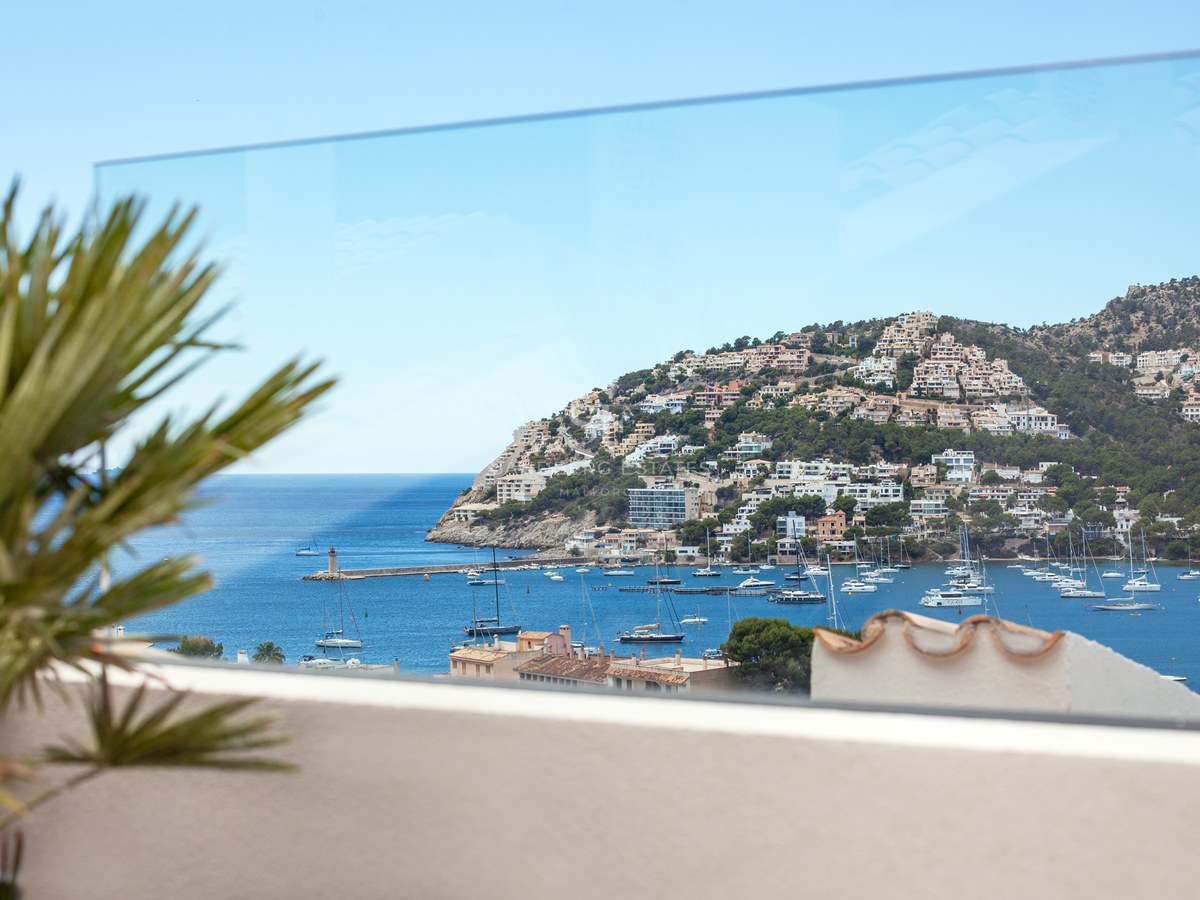 View through a glass balcony railing of a Mediterranean harbor filled with boats and a hillside town.