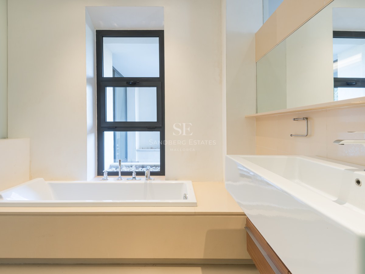 Modern bathroom featuring a built-in white bathtub next to a window and a large white rectangular sink with a wide mirror.