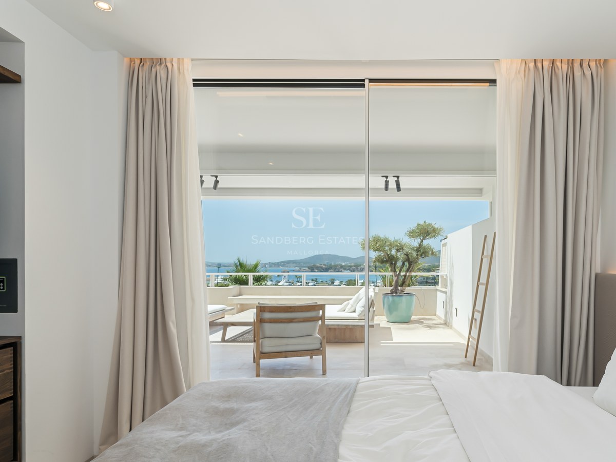 Chambre lumineuse avec baies vitrées s'ouvrant sur une terrasse ensoleillée offrant une vue sur la mer.