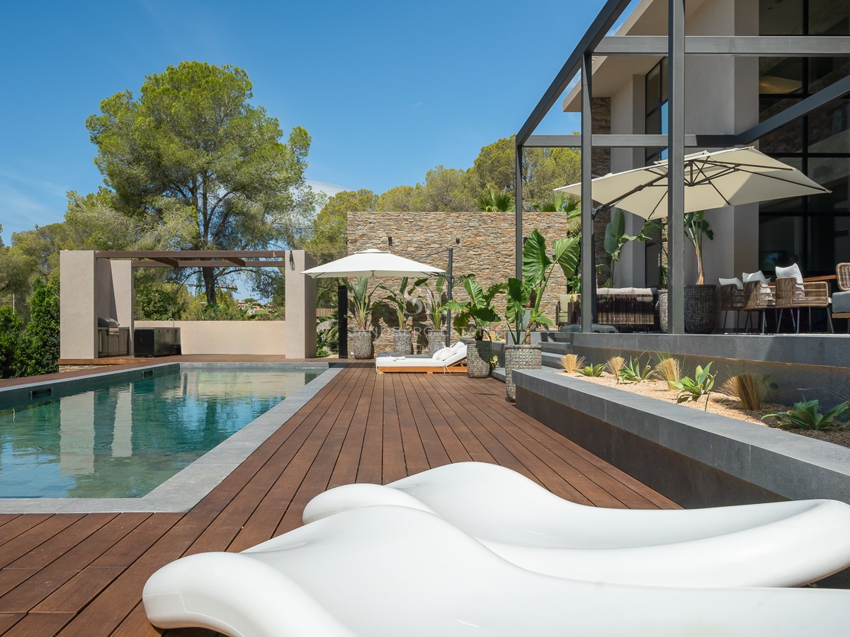 Piscine extérieure de luxe avec terrasse en bois, bains de soleil blancs et murs en pierre sous un ciel bleu.
