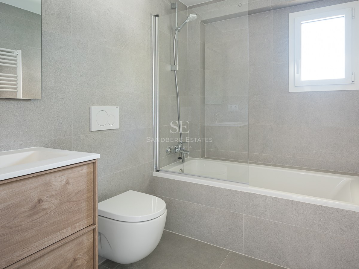 Salle de bain contemporaine avec carrelage gris effet pierre, baignoire et paroi en verre, et meuble sous vasque en chêne.