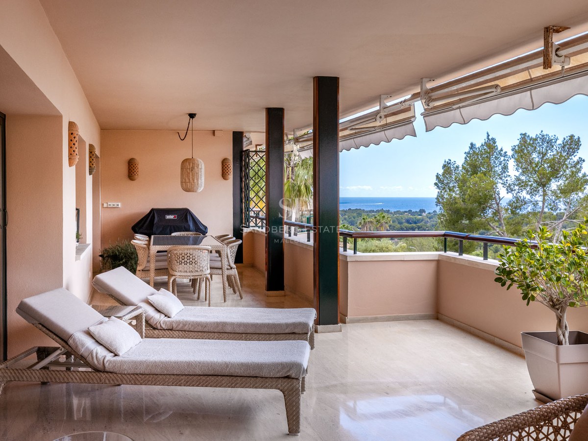 Terrasse couverte avec bains de soleil, salle à manger extérieure et vue sur la mer et la verdure.