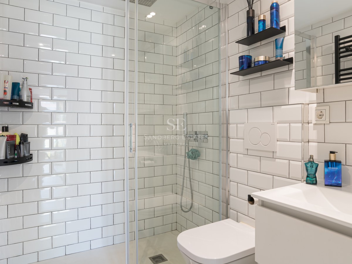 Baño moderno con azulejos blancos tipo metro, ducha de cristal, radiador negro y lavabo minimalista.