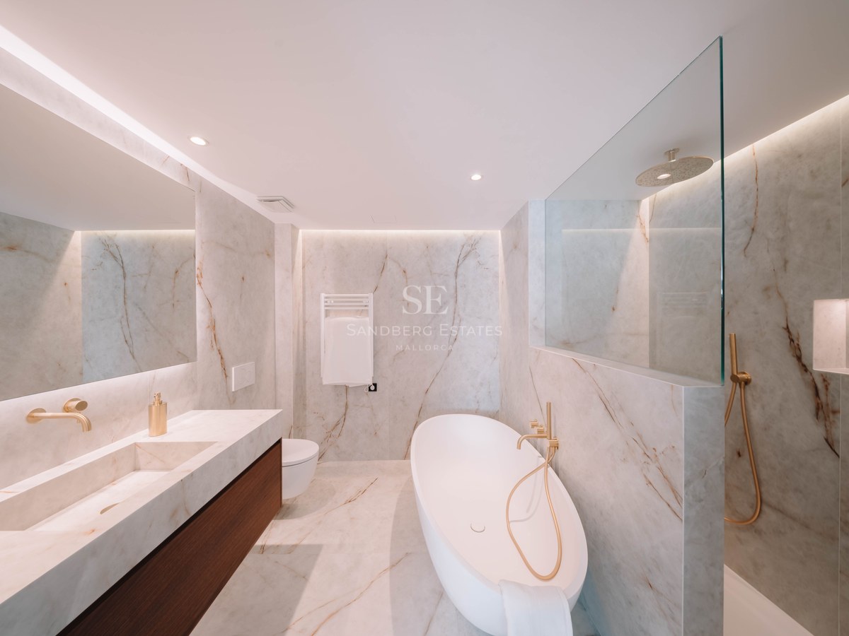 Salle de bain moderne en marbre avec baignoire îlot blanche, robinetterie dorée et double vasque.