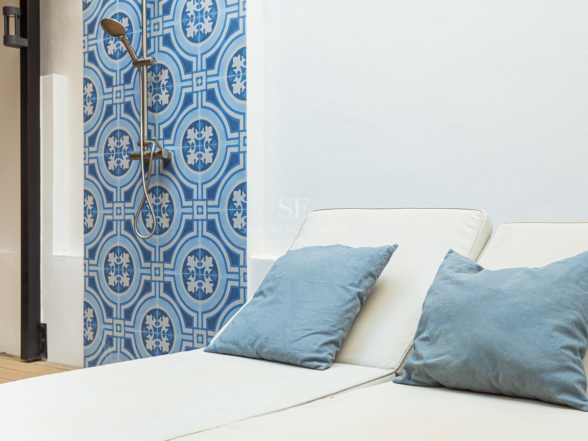 Tumbona con cojines azules junto a una pared de azulejos azules estampados y una moderna ducha exterior.