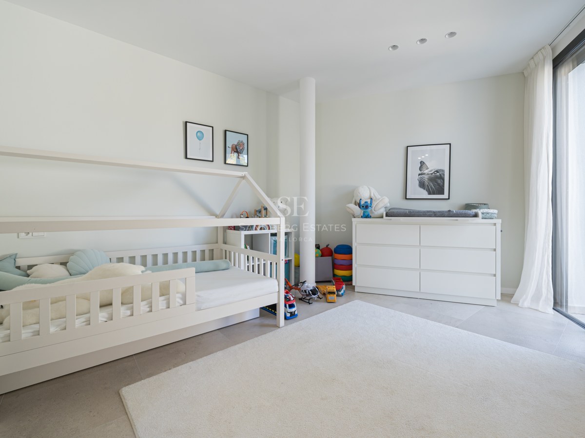 Chambre d'enfant moderne avec lit cabane blanc, commode et grandes baies vitrées avec voilages.