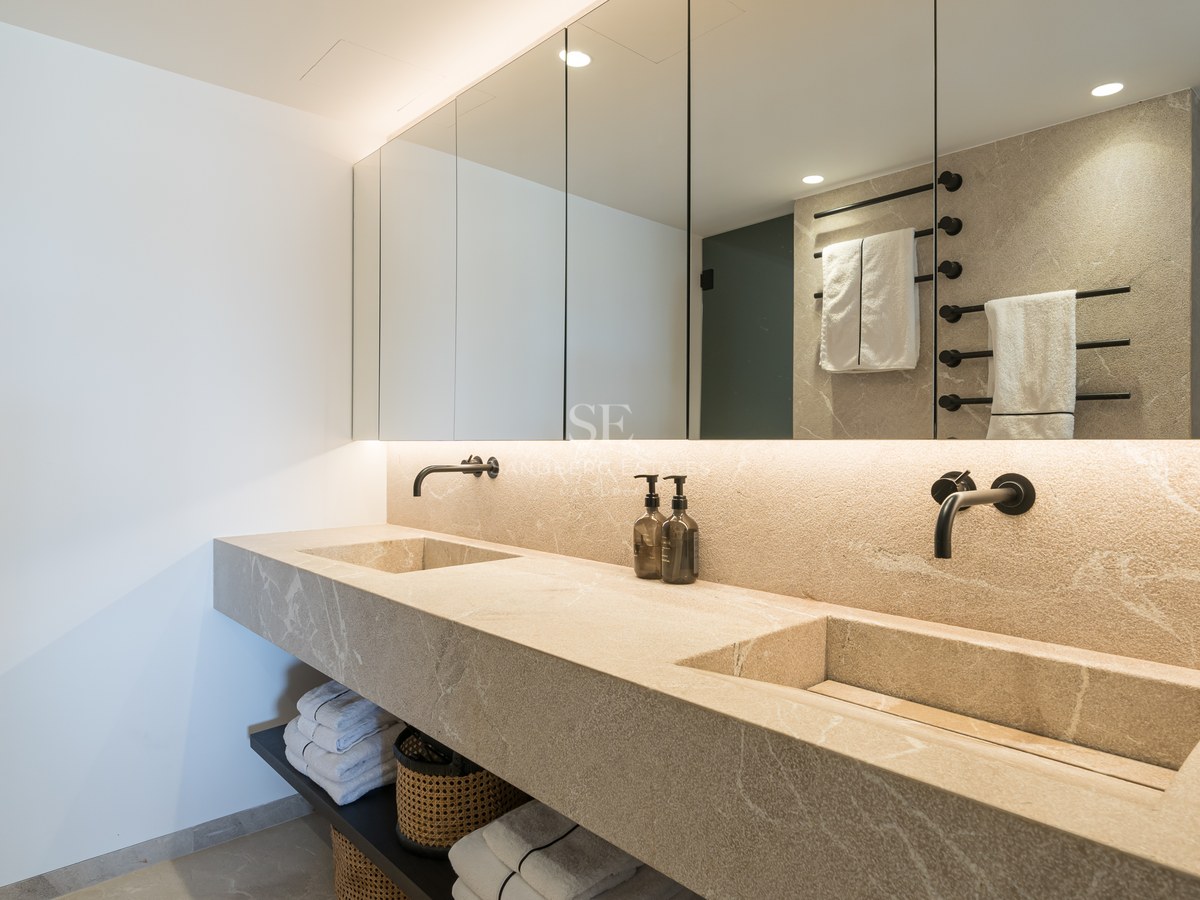 Salle de bain de luxe avec double vasque intégrée en pierre, miroirs rétroéclairés et robinetterie noire mate.