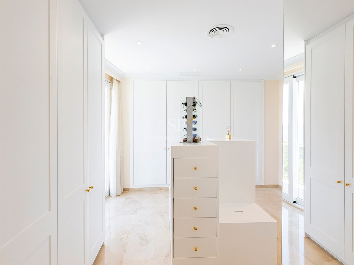 Spacious white walk-in closet featuring floor-to-ceiling built-in wardrobes, a central island, and polished marble floors.