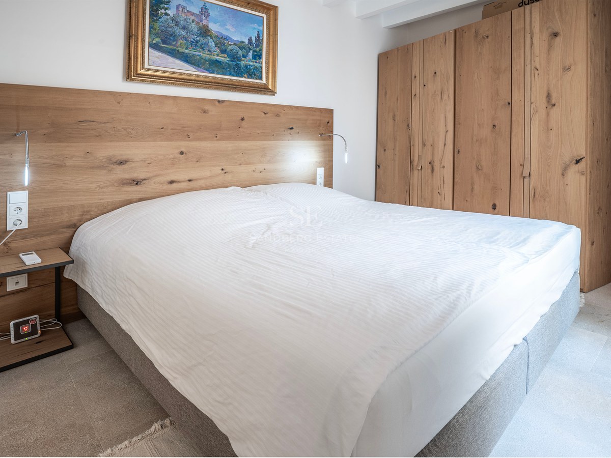 Modern bedroom with a large bed, light wood headboard and wardrobe, and a classic landscape painting.