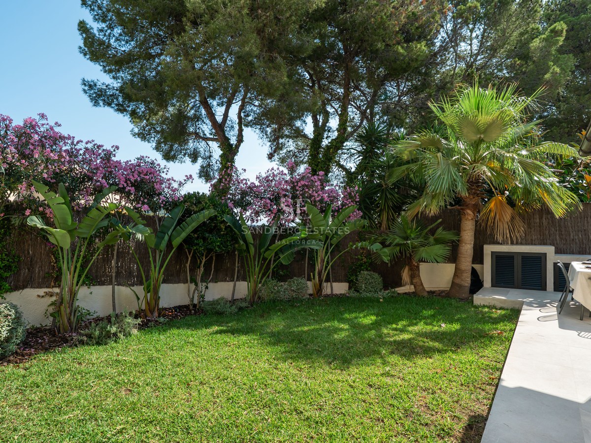 Jardin privé avec pelouse impeccable, plantes tropicales et terrasse en pierre avec table à manger ensoleillée.