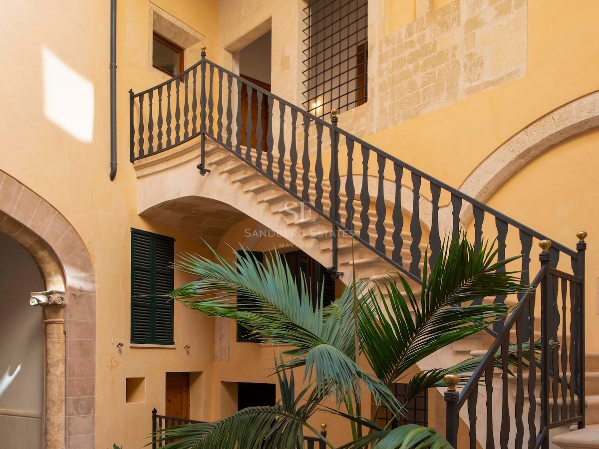 Traditional courtyard with yellow walls, a stone staircase with iron railings, and a central palm tree.