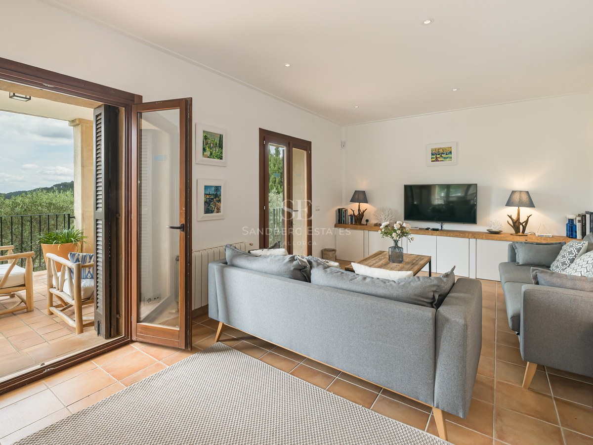 Modern grå soffa i ett vardagsrum med terrakottagolv och öppna trädörrar mot en terrass.