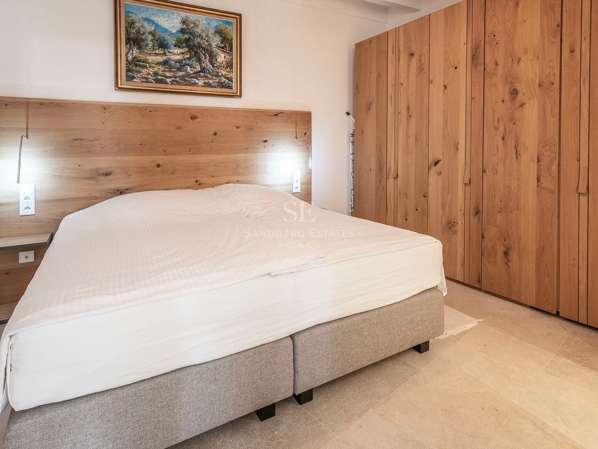 A modern bedroom featuring a large bed with a wooden headboard, extensive oak wardrobes, and a painting on the wall.