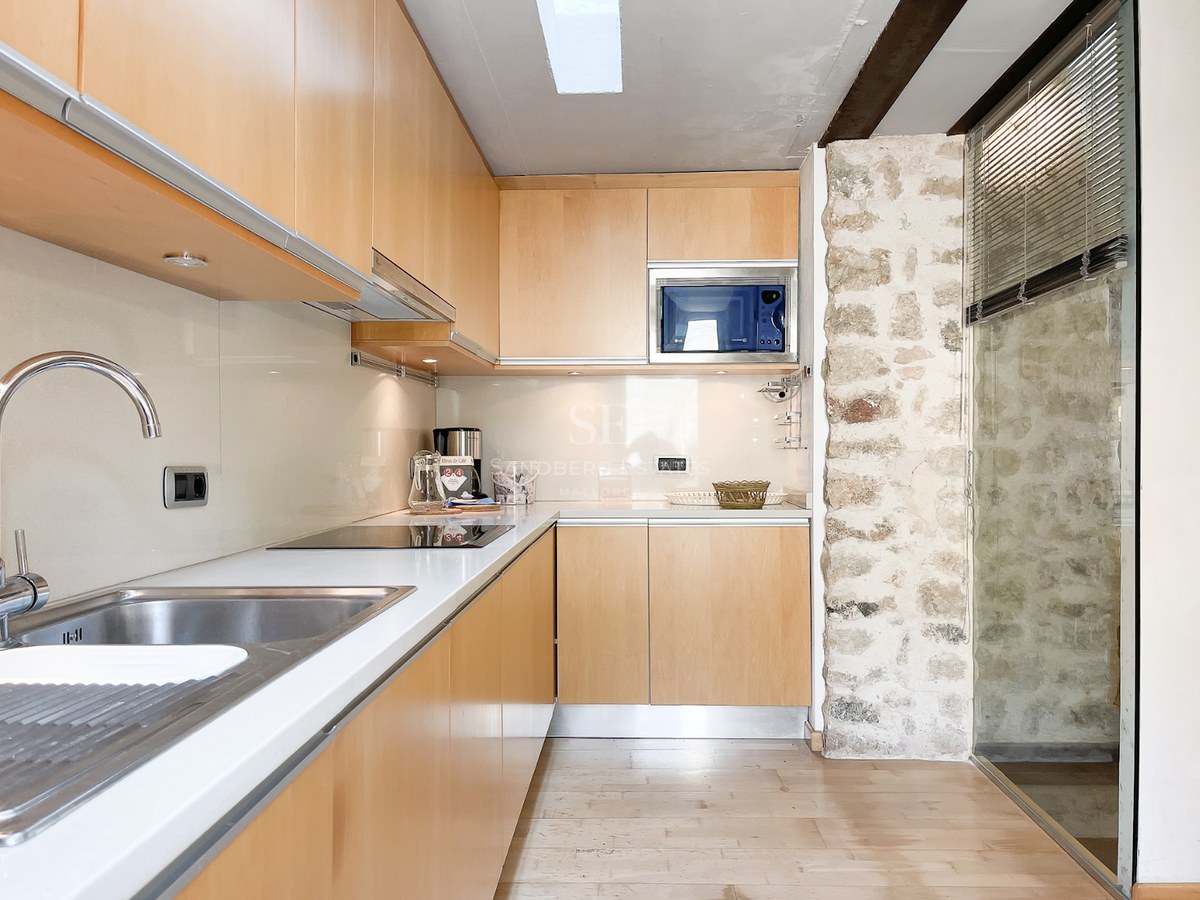 Cocina moderna con armarios de madera clara, encimera blanca y una pared de acento en piedra natural.