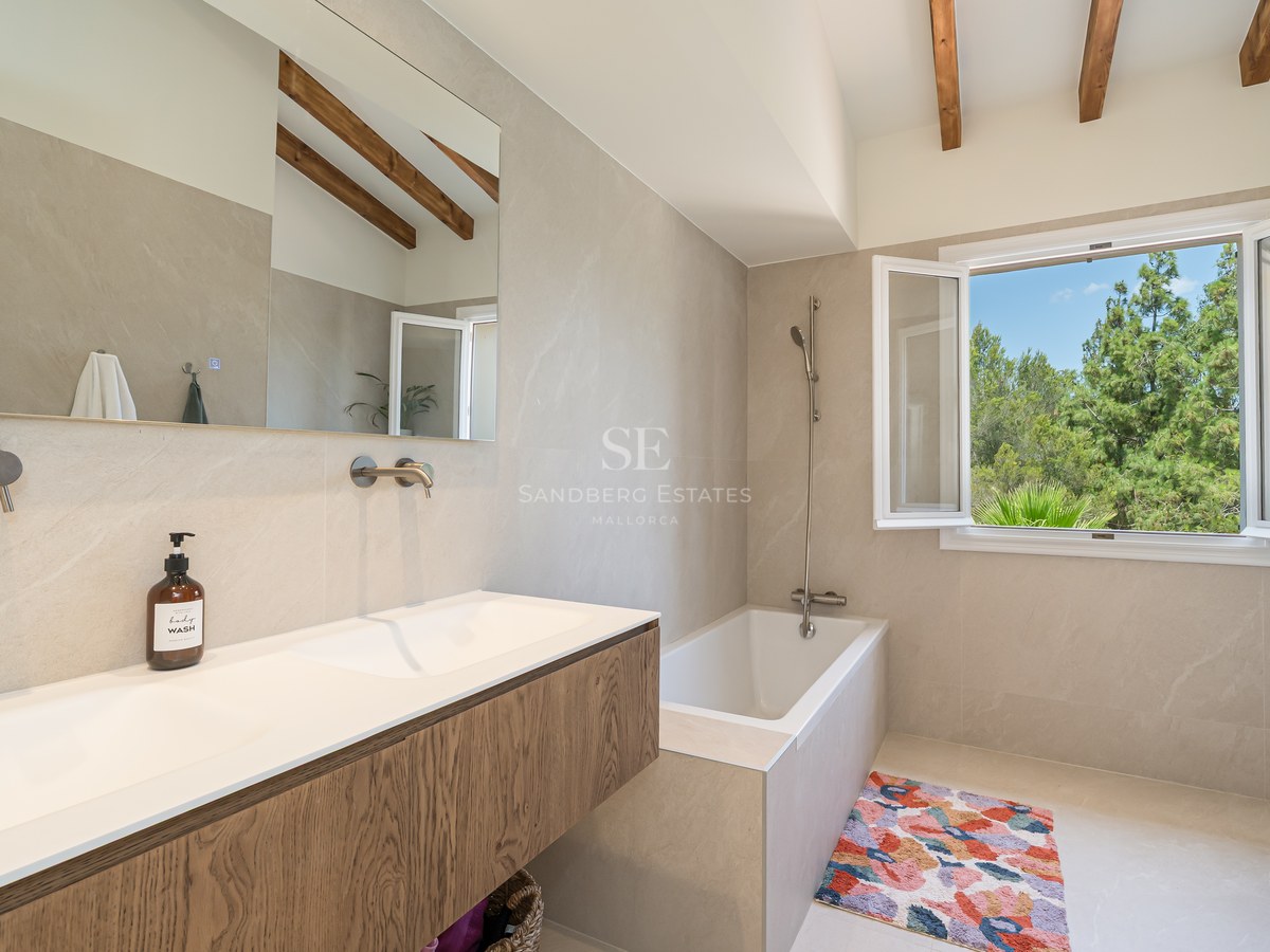 Contemporary bathroom featuring a wood vanity, double sink, and views of pine trees through an open window.