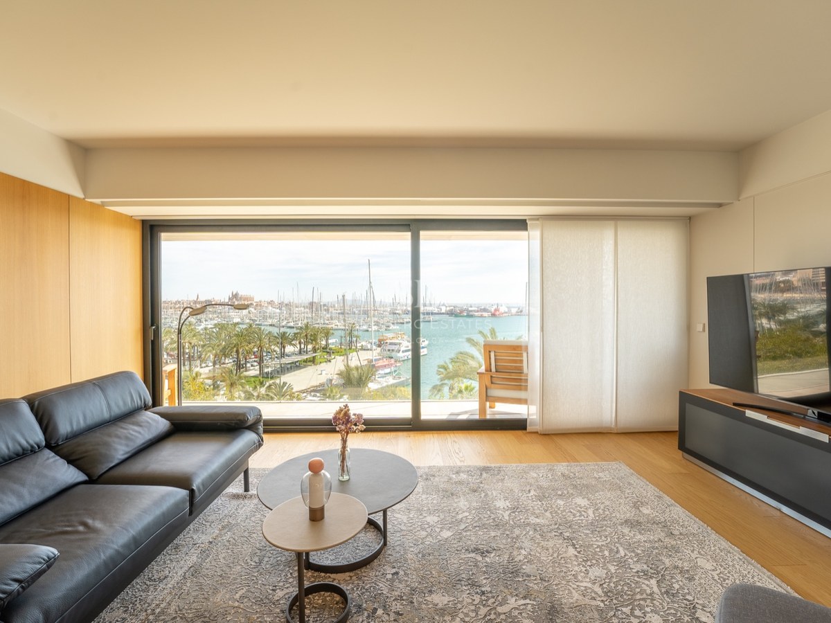 Salon contemporain avec canapé en cuir noir et grande baie vitrée offrant une vue sur un port de plaisance.