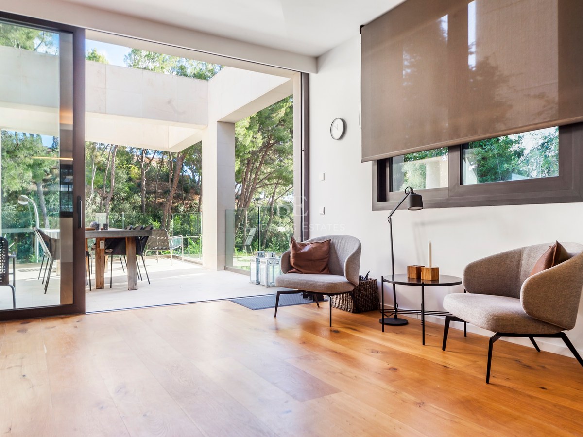 Coin salon moderne avec deux fauteuils gris sur parquet en chêne, s'ouvrant sur une terrasse ensoleillée.