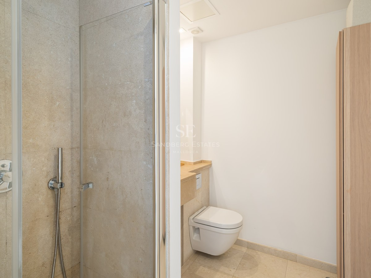 Bathroom featuring a glass walk-in shower, wall-mounted toilet, and beige stone walls.