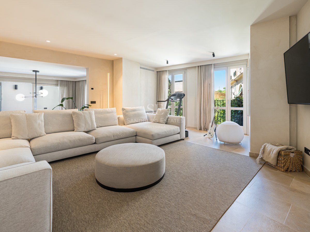 Bright living room featuring a large cream sectional sofa, beige rug, and wall-mounted flat-screen TV.