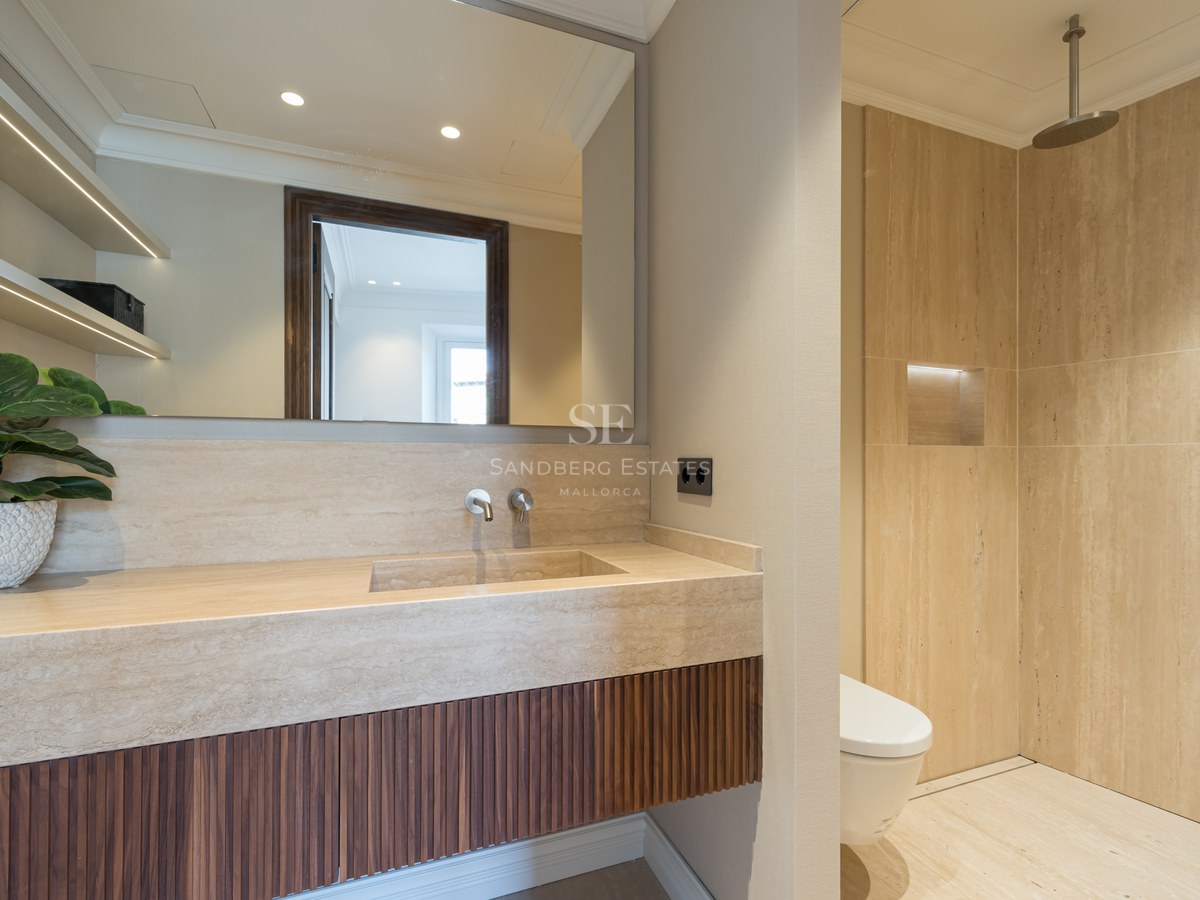 Baño moderno con lavabo de travertino, mueble de madera alistonada y ducha de obra con efecto lluvia.
