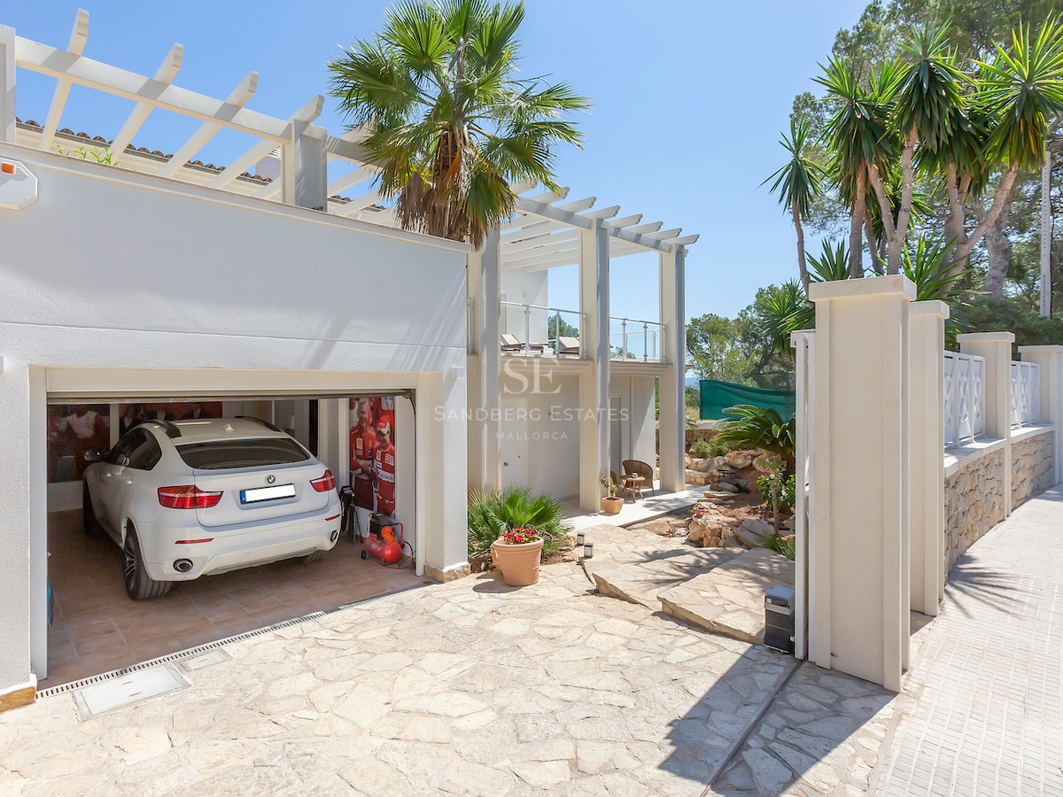 Exterior of a white luxury villa featuring a stone driveway, a white pergola, and an open garage with a luxury SUV.