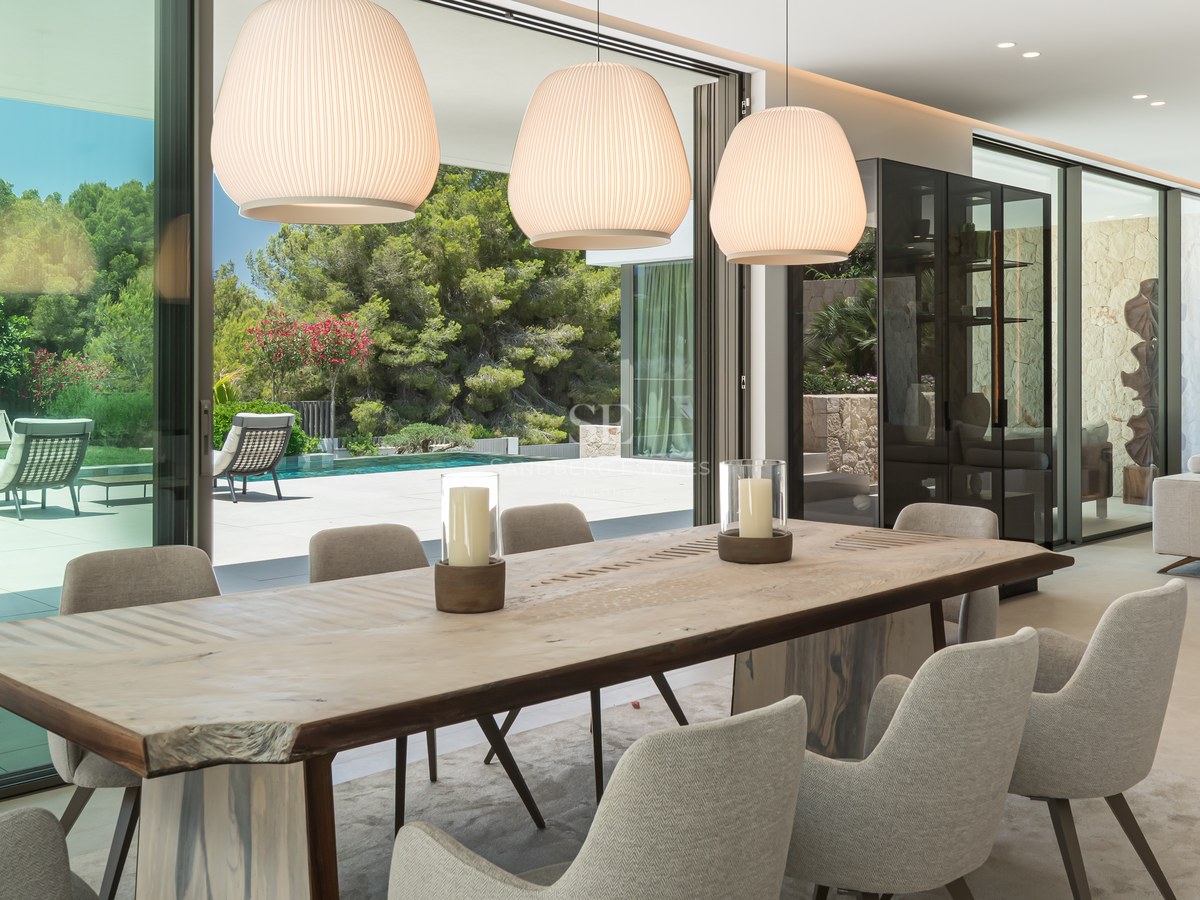 Salle à manger moderne avec table en bois naturel et chaises rembourrées donnant sur une piscine à travers des baies vitrées.