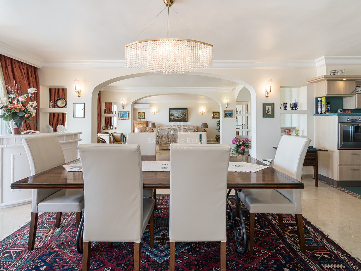 Bright dining room with marble floors, a crystal chandelier, dark wood table, and arches leading to the lounge.