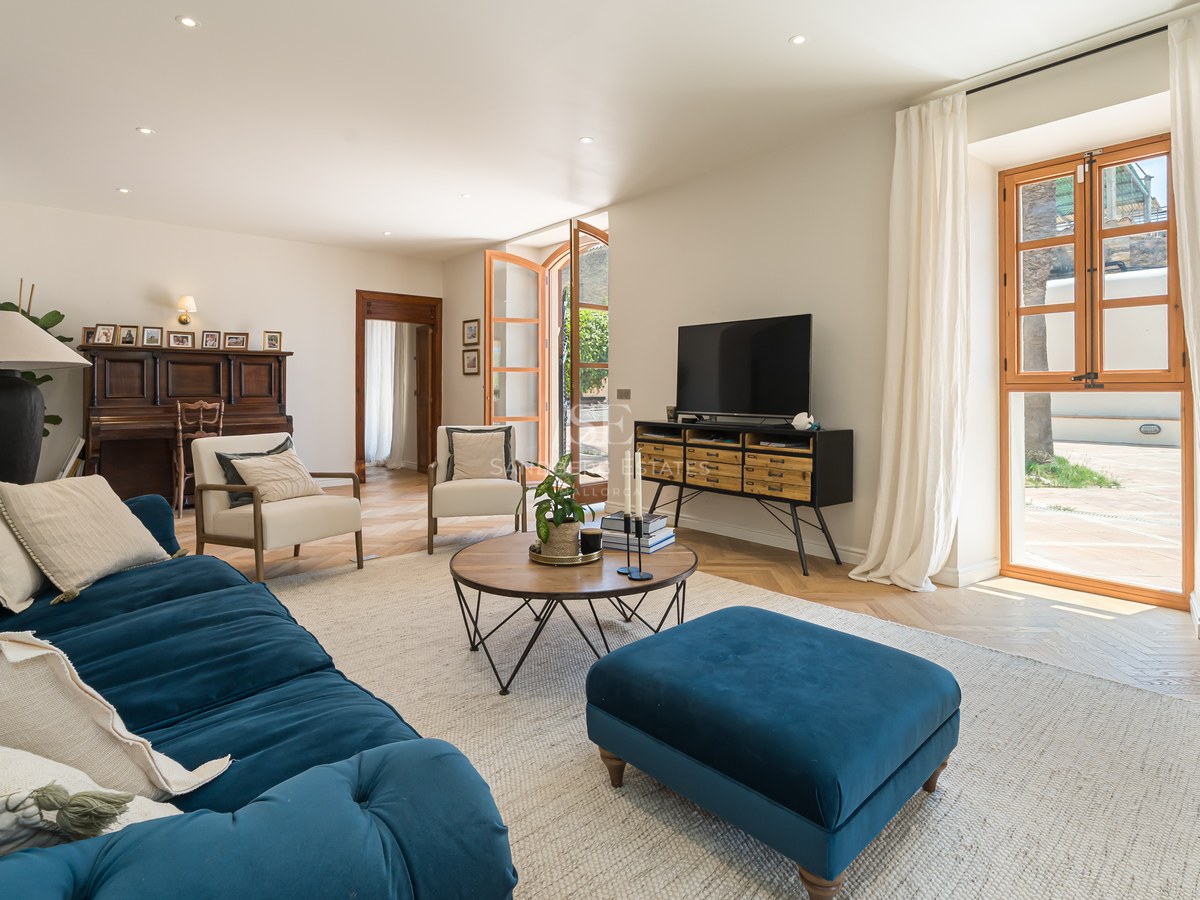 Spacious living room featuring a teal velvet sofa, oak herringbone floors, and large wooden-framed windows to a terrace.