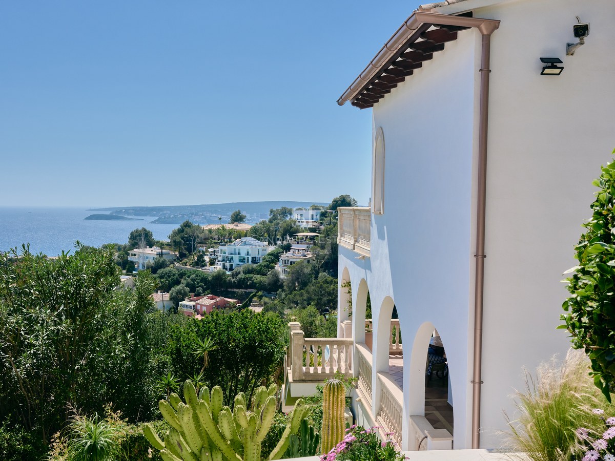 Side view of a white Mediterranean villa with arched terraces overlooking the coast and blue sea.