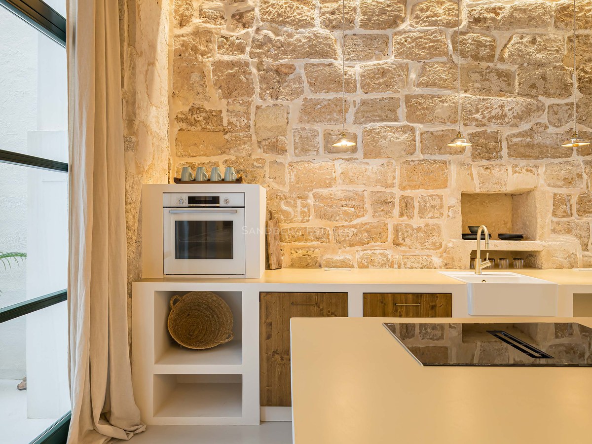 Cuisine moderne avec mur en pierre rustique, comptoirs blancs, accents en bois et îlot avec plaque de cuisson.