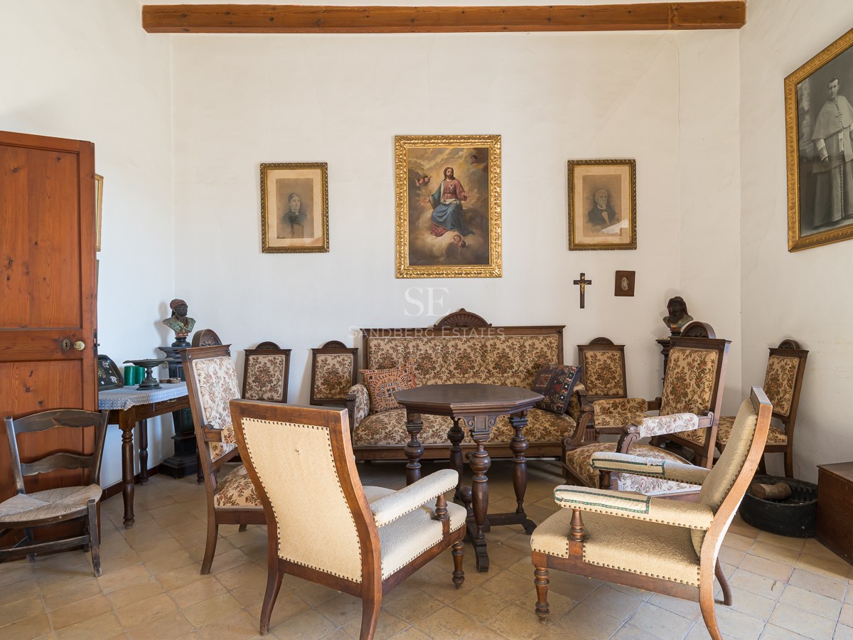 Sala de estar clásica con muebles de madera antiguos, tapicería estampada, pinturas religiosas y suelo de baldosas.