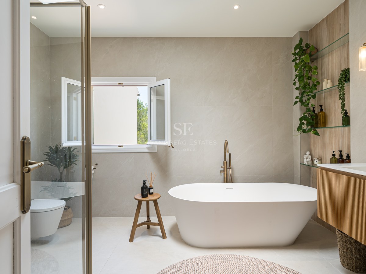 Modern bathroom featuring a white freestanding bathtub, brushed brass fixtures, stone-tiled walls, and an oak vanity.