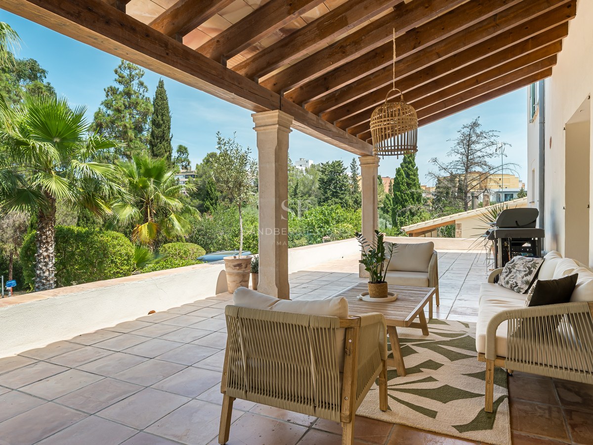 Mediterranean terrace with wooden beam ceiling, terracotta floor, outdoor lounge furniture, and views of palm trees.
