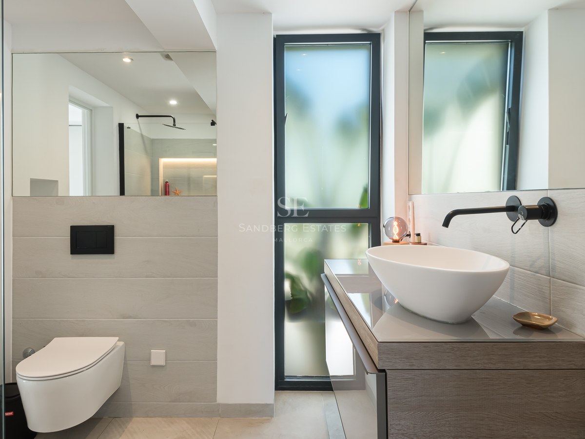 Contemporary bathroom featuring a white vessel sink, matte black faucet, wall-mounted toilet, and large mirrors.