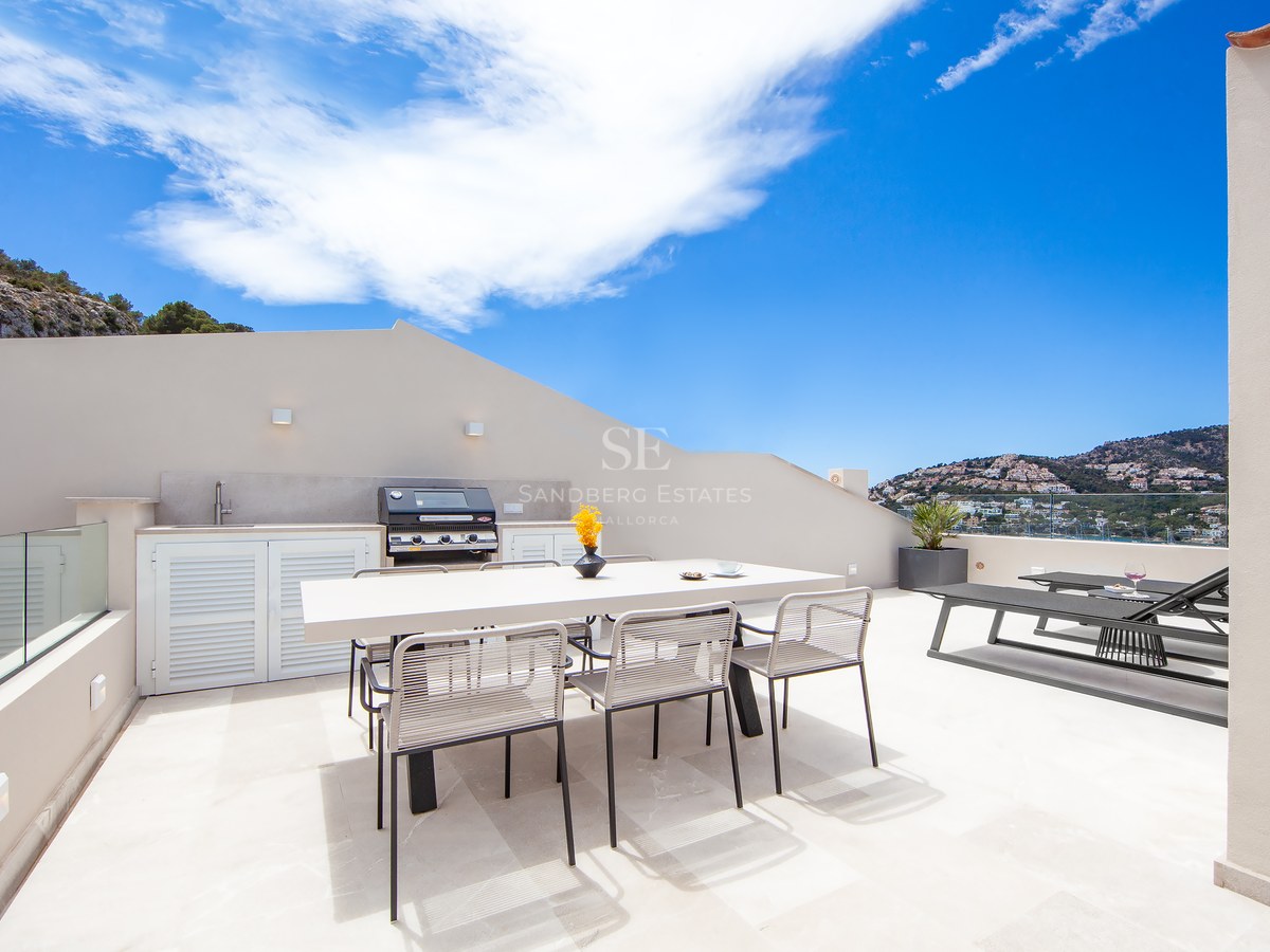 Modern rooftop terrace featuring an outdoor kitchen, dining table, and sun loungers with panoramic coastal views.