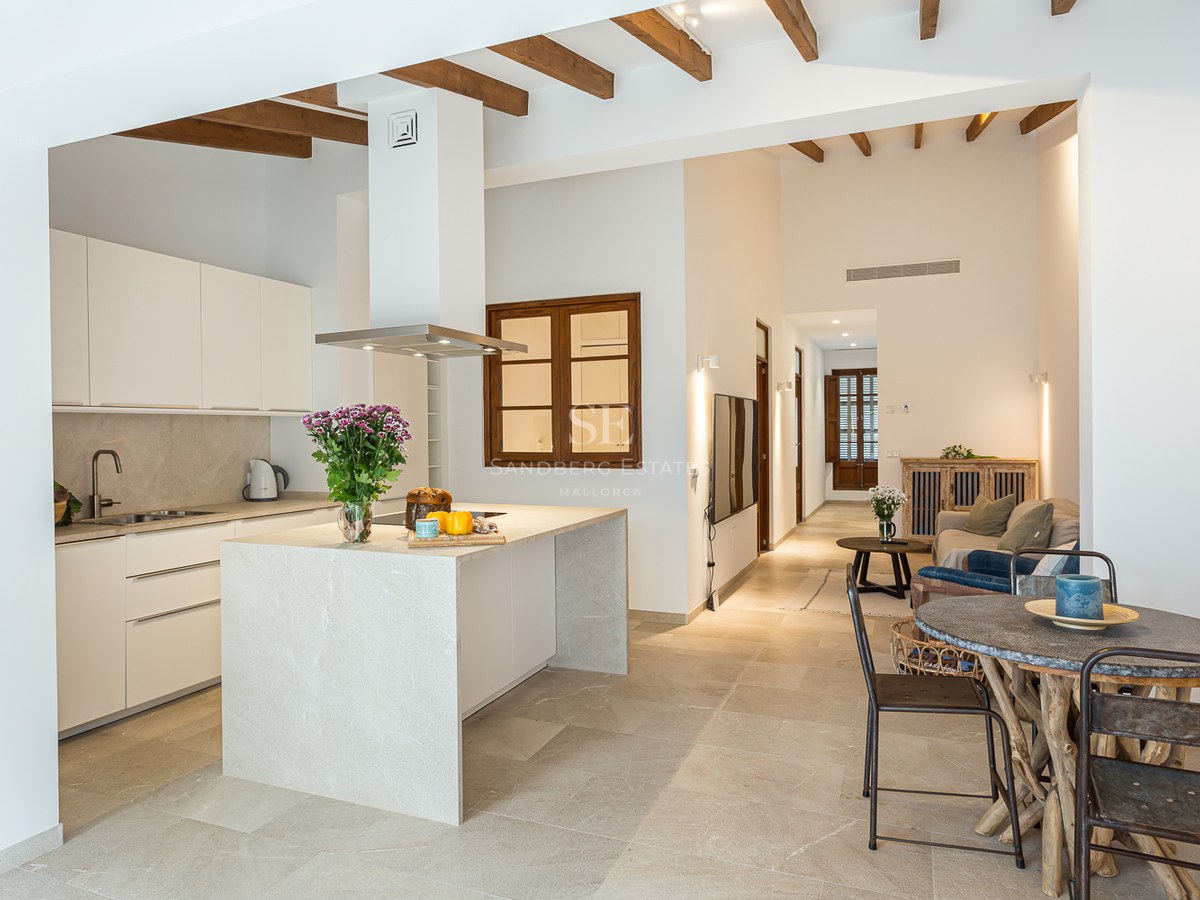 Cocina luminosa con isla de piedra, vigas de madera en el techo y zona de comedor rústica.