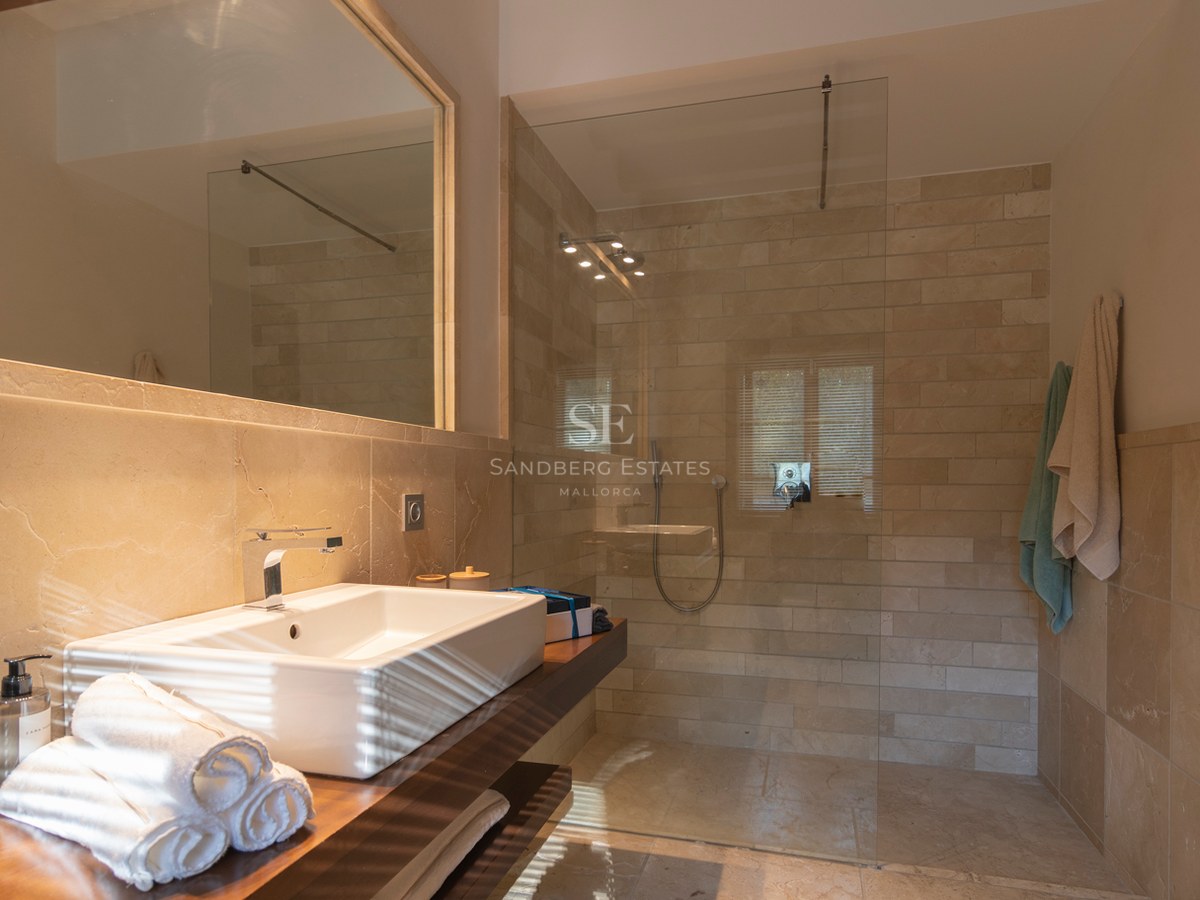 Salle de bain contemporaine avec douche en verre, pierre naturelle et vasque sur plan de travail en bois.