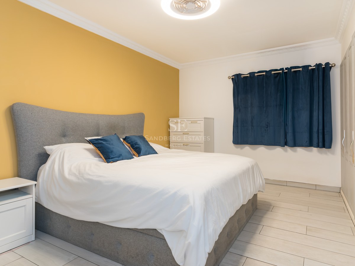 A bright bedroom featuring a gray bed, yellow accent wall, white built-in wardrobes, and dark blue curtains.