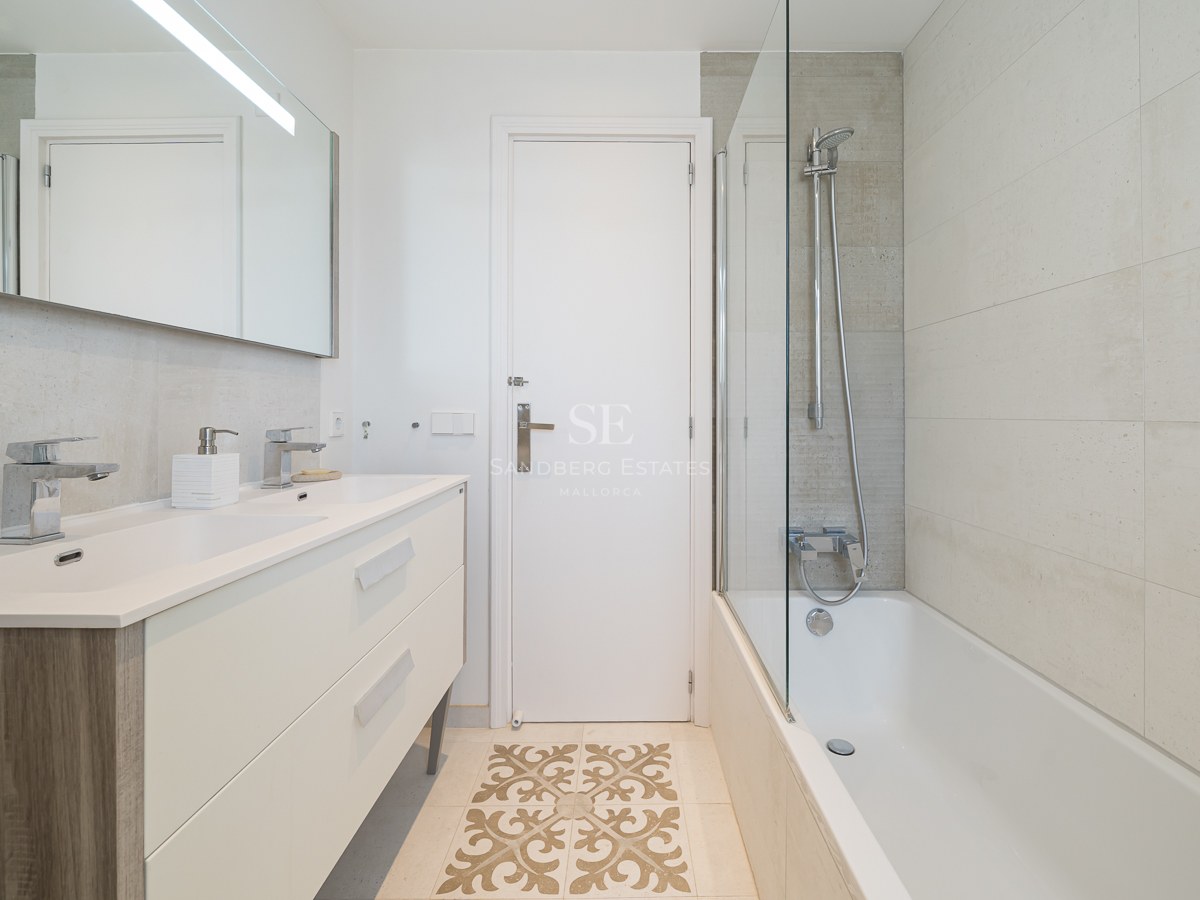 Salle de bain moderne avec double vanité crème, baignoire avec paroi vitrée et carrelage décoratif au sol.