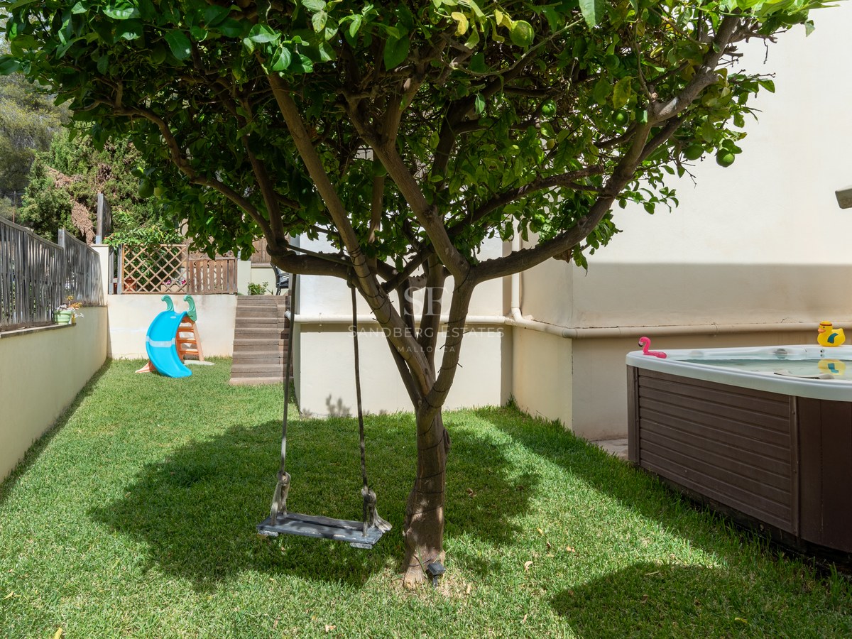 Jardín con césped, columpio en un árbol, tobogán azul y jacuzzi exterior revestido de madera.