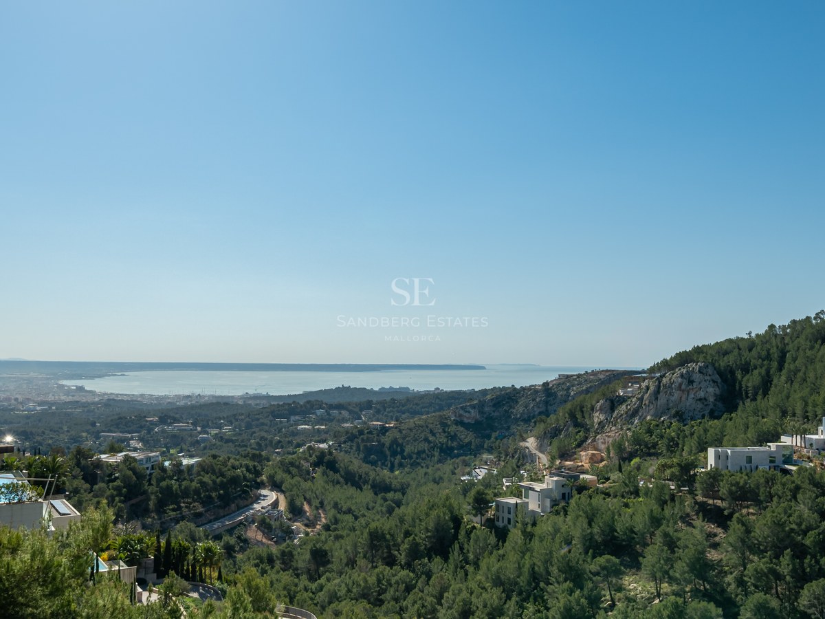 Villas blancas modernas entre pinos con vistas al mar Mediterráneo bajo un cielo azul despejado.